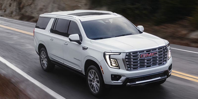 2026 GMC Yukon XL driving on a scenic highway showcasing its bold exterior design in Kewanee, IL